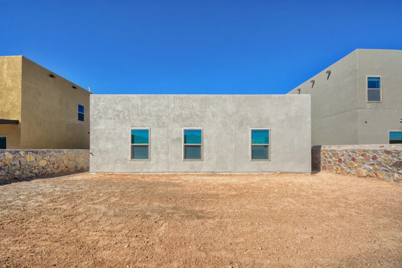 Rear exterior of modern stucco home with three windows and dirt backyard