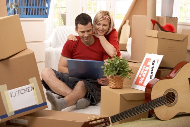 Couple with laptop surrounded by moving boxes.