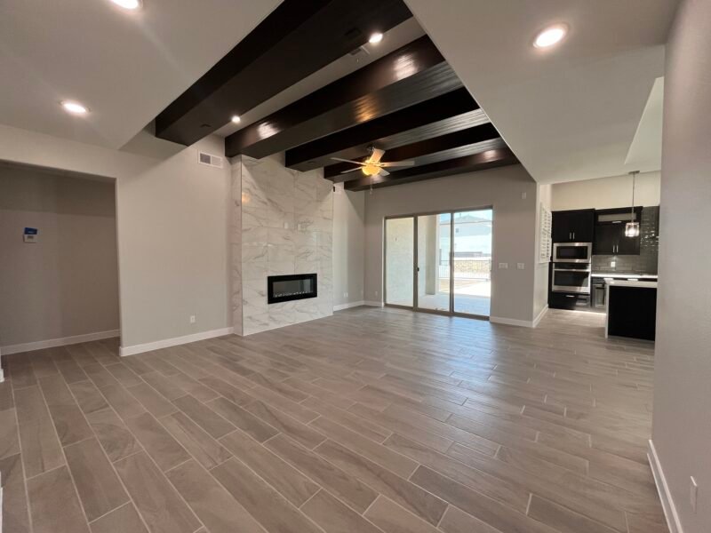 Open living room with fireplace, wood‑look floors, and ceiling beams