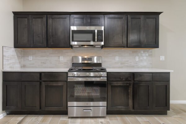 A kitchen wall with dark wood cabinets, a stainless stove and microwave, and light tile backsplash