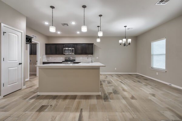 A new open kitchen and dining area with a large island, pendant lights, and wood‑look tile flooring.
