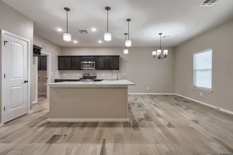 A new open kitchen and dining area with a large island, pendant lights, and wood‑look tile flooring.