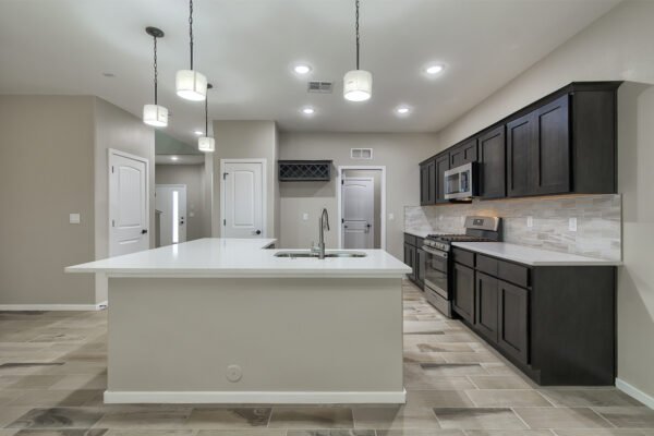 A modern kitchen with a large white island, dark wood cabinets, and pendant lights