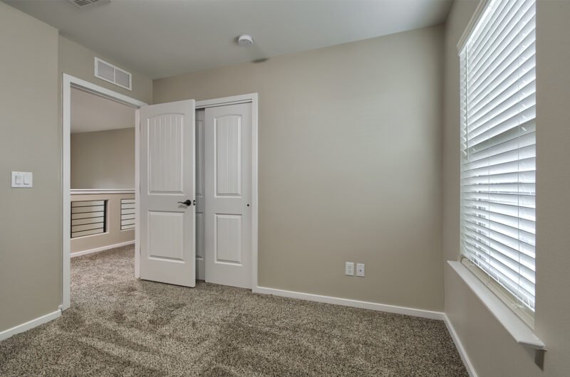 A small empty bedroom with carpet, an open white door, and a window with blinds