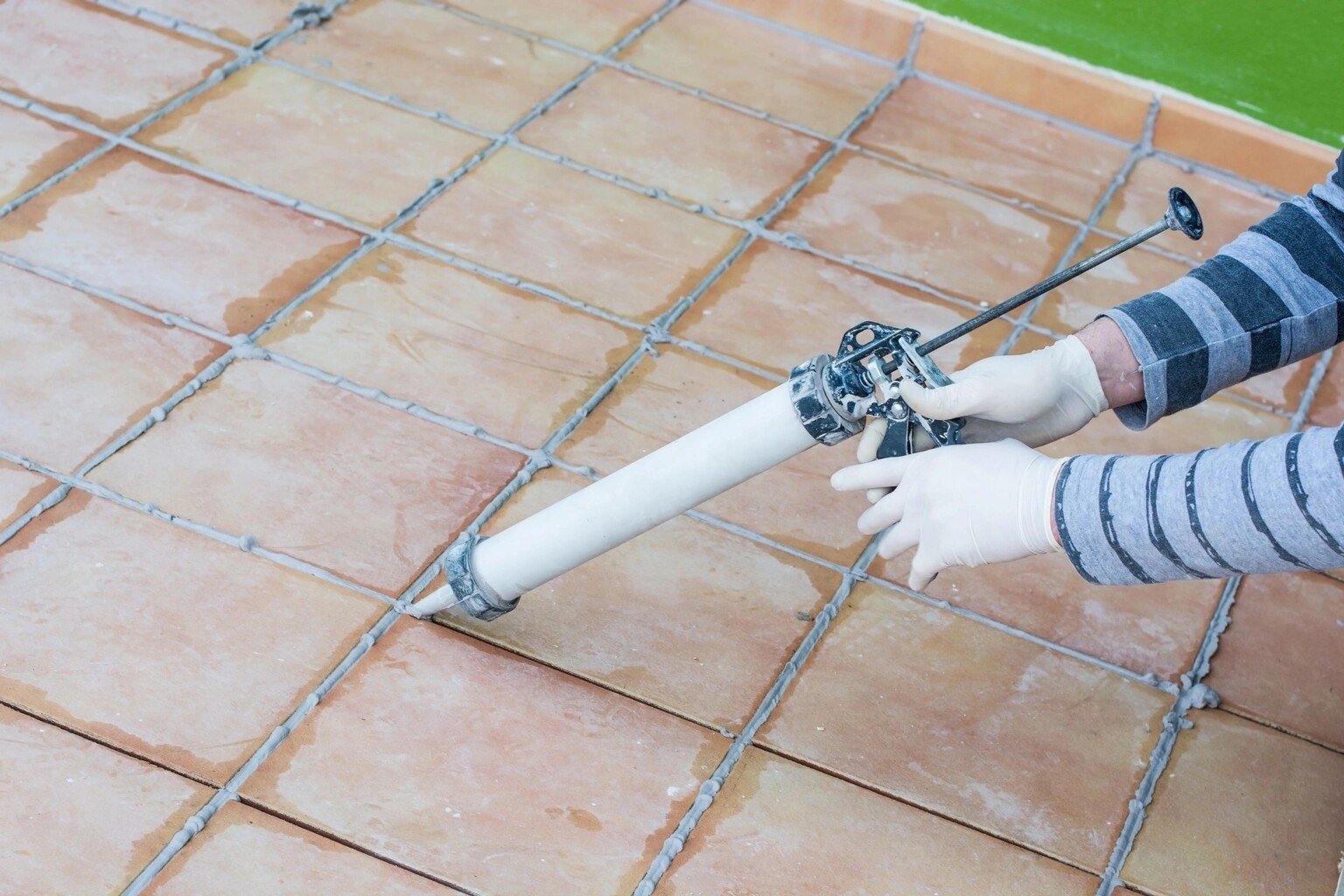 Person applying grout between floor tiles