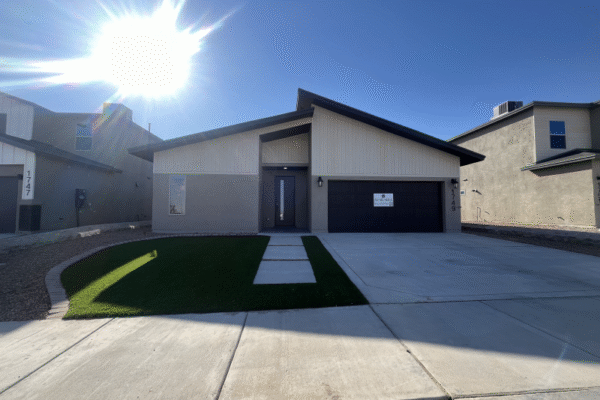 A single‑story new home exterior with front lawn, concrete driveway, and bright sun overhead