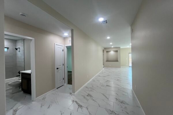 Hallway interior with tile floor, bathroom doorway, and open living area