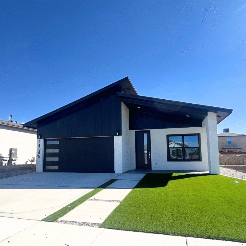 Modern single‑story house exterior with black garage door and green lawn