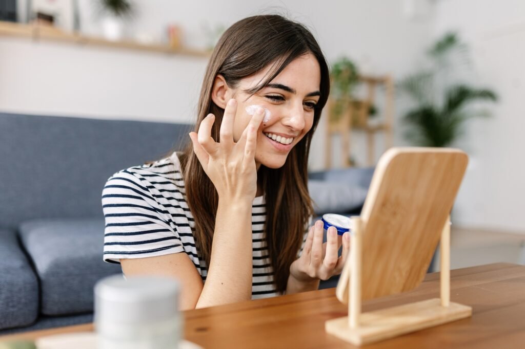 Smiling young pretty woman applying skin cream at her face